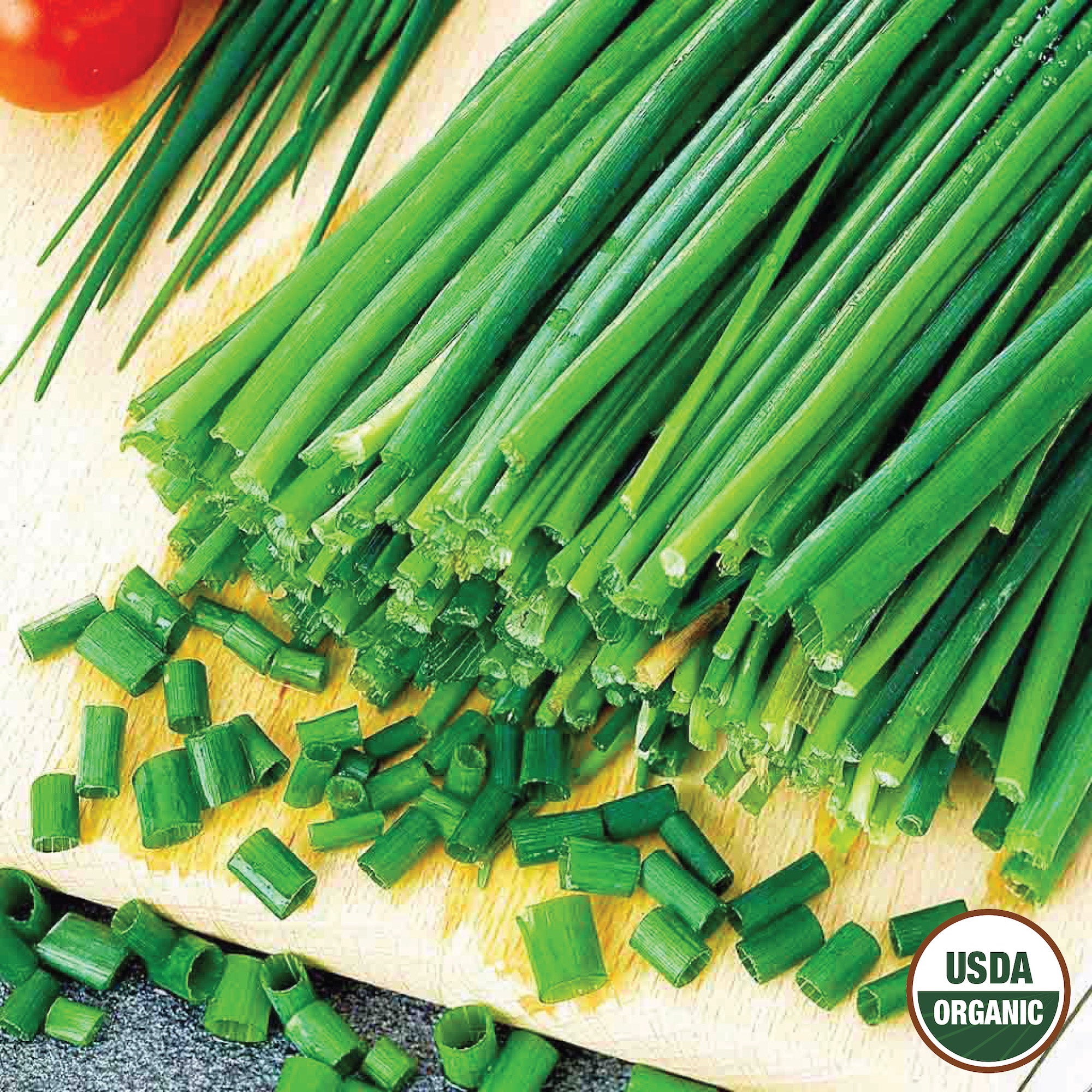 A bunch of fresh green chives with both whole stalks and chopped leaves displayed on a wooden surface, featuring a USDA Organic label.